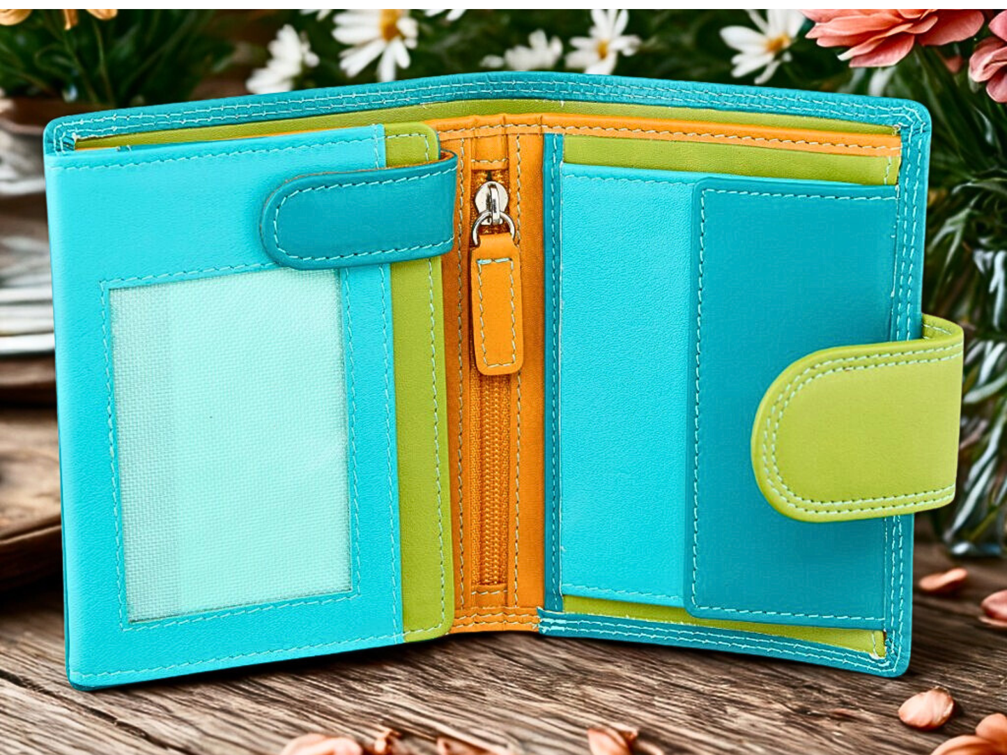 Turquoise wallet with orange and green accents on a wooden surface with flowers in the background